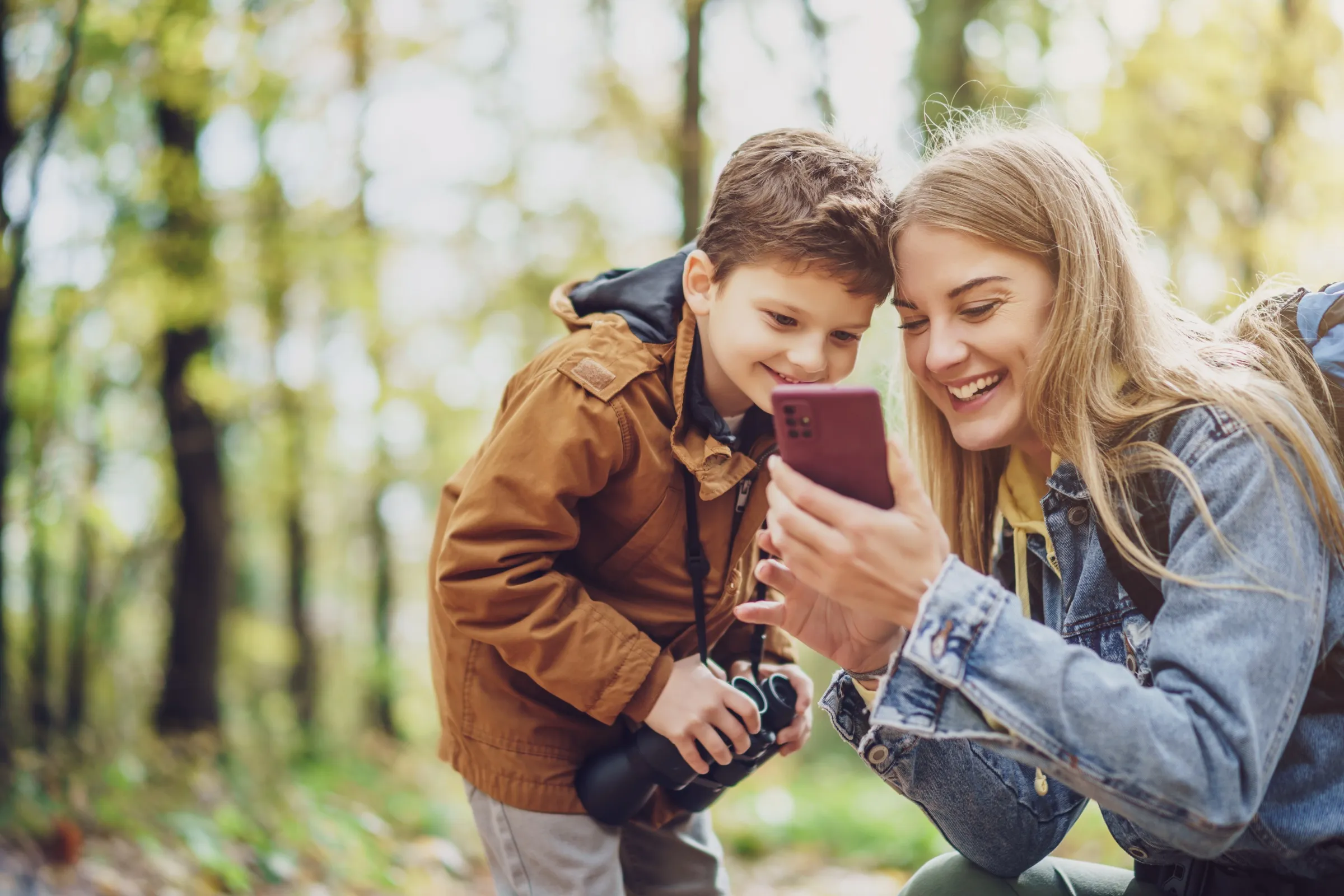 Ein Kind und eine Erwachsene schauen im Wald gemeinsam auf ein Smartphone